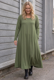 Blond modell i grön Ballerina Long Sleeve, gående längs träfasaden